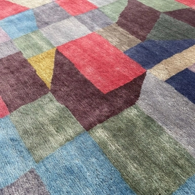 A custom handmade rug inspired by Paul Klee’s painting “Fire at Full Moon,” featuring vibrant geometric patterns in red, green, blue, and yellow tones with intricate textures.