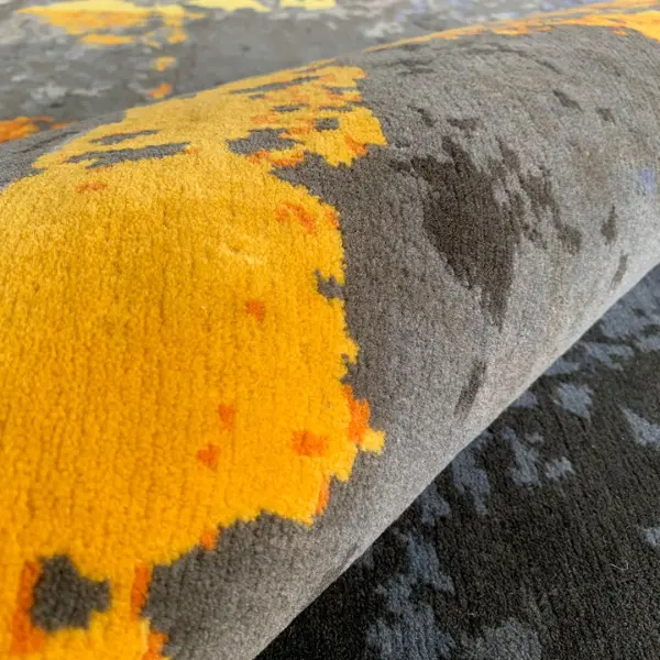 Gros plan sur un tapis fait main sur mesure en gris et jaune d'après la photo d'un sol d'usine du client.