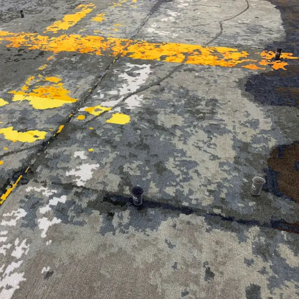 Gros plan sur un tapis fait main sur mesure en gris et jaune d'après la photo d'un sol d'usine du client.