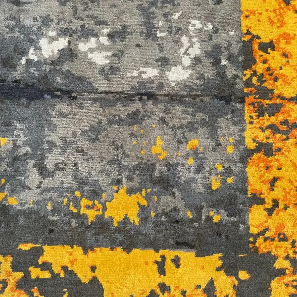 Gros plan sur un tapis fait main sur mesure en gris et jaune d'après la photo d'un sol d'usine du client.