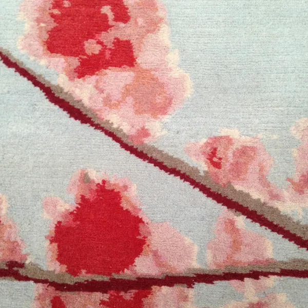 Gros plan sur un tapis fait sur mesure pour compléter un salon d'inspiration japonaise, avec des fleurs de cerisier en gris et en rose.