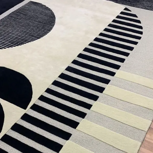 Gros plan sur un tapis fait main pour un projet de décoration d'intérieur, noir et crème, avec des rayures et des demi-cercles, différentes textures et hauteurs de poils.