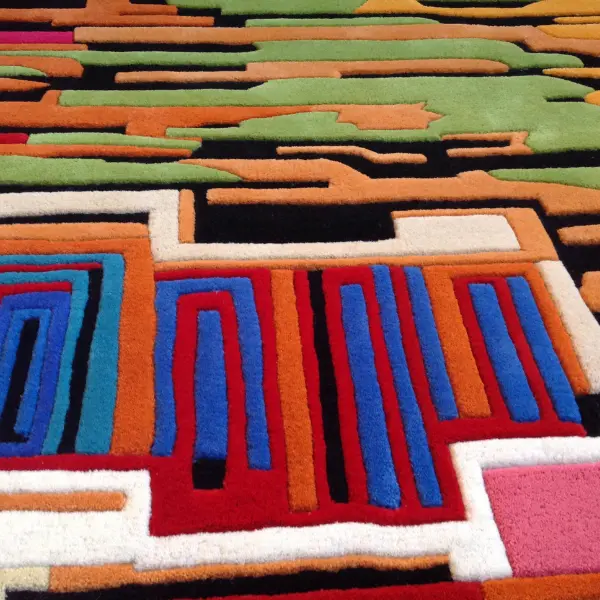 Gros plan sur un tapis tufté à la main avec différentes hauteurs de poils et des lignes arrondies, très coloré rappelant une ville imaginaire