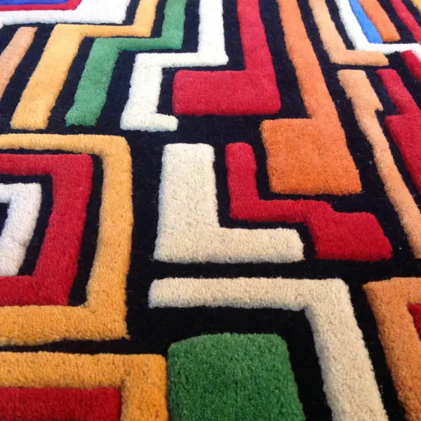 Gros plan sur un tapis tufté à la main avec différentes hauteurs de poils et des lignes arrondies, très coloré rappelant une ville imaginaire