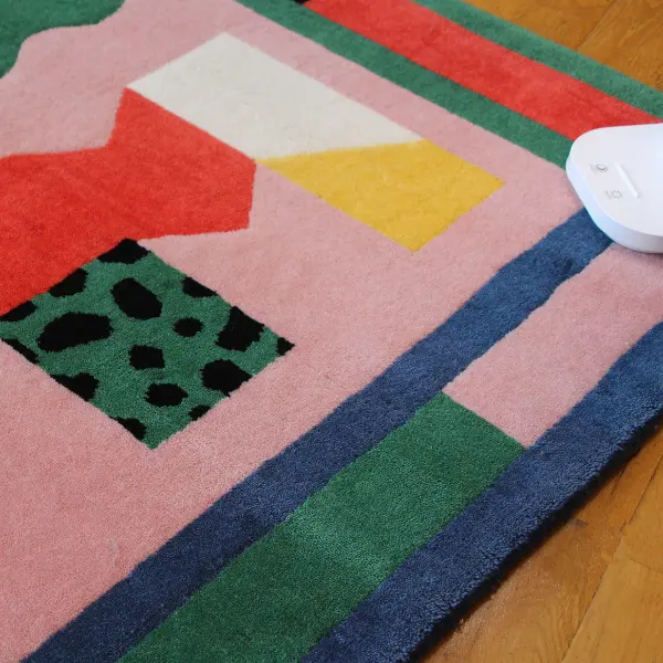 Gros plan sur un tapis noué à la main, rose et coloré, avec des lettres graphiques dessinées par l'artiste italienne Camilla Falsini