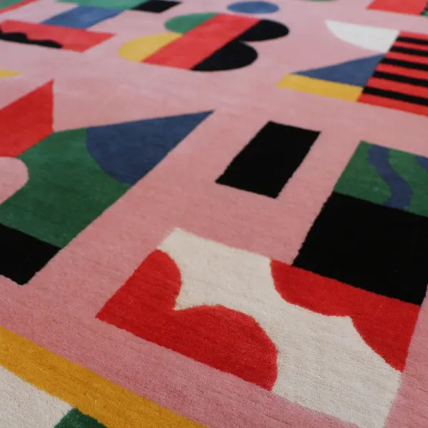 Gros plan sur un tapis noué à la main, rose et coloré, avec des lettres graphiques dessinées par l'artiste italienne Camilla Falsini