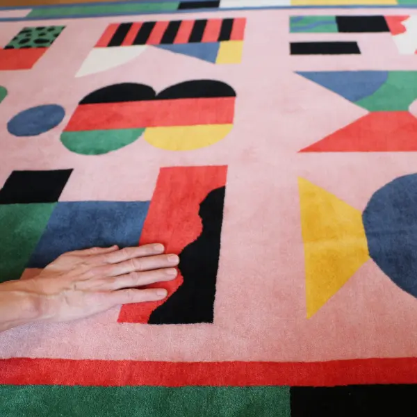 Gros plan sur un tapis noué à la main, rose et coloré, avec des lettres graphiques dessinées par l'artiste italienne Camilla Falsini