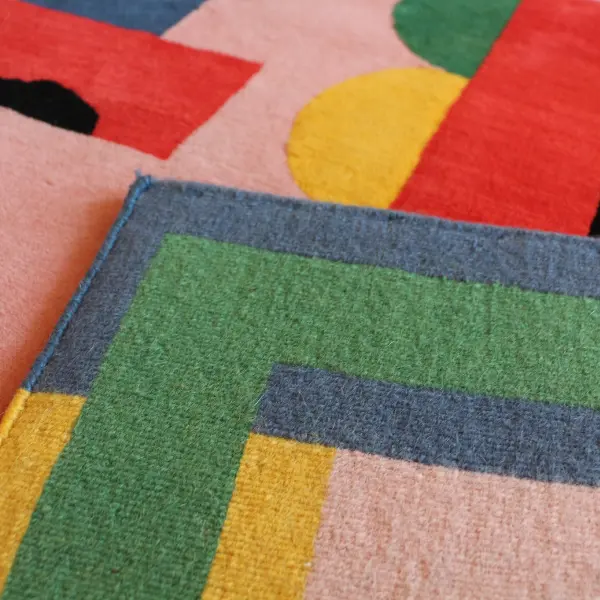 Gros plan sur un tapis noué à la main, rose et coloré, avec des lettres graphiques dessinées par l'artiste italienne Camilla Falsini